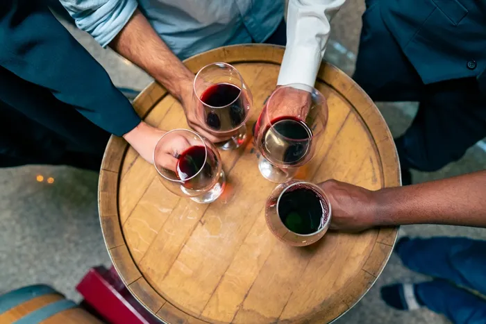 Men standing around a round table and holding glasses of wine in their hands