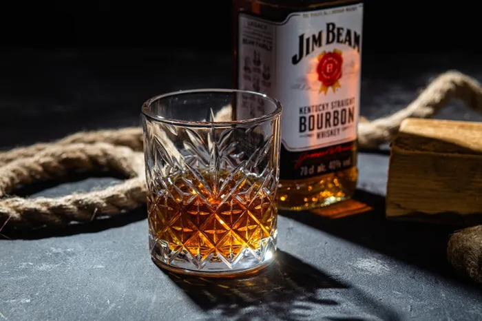 A glass of neat Jim Bean Bourbon next to a fresh bottle and thick rope